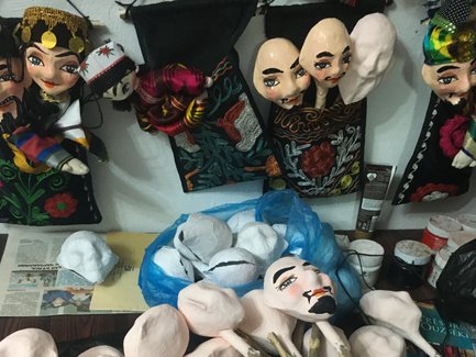 Eine Vielzahl von Puppen und Puppenköpfen liegt auf einem Tisch, umgeben von bunten Stoffen und Materialien.