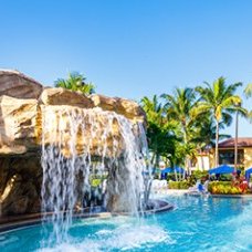 Ein malerischer Pool mit einem Wasserfall, umgeben von Palmen und Sonnenliegen, ideal für Entspannung und Erholung.