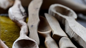 Eine Sammlung von handgefertigten Holzlöffeln und -messern liegt auf einem grünen Tuch, das die Kunst des Schnitzens zeigt.