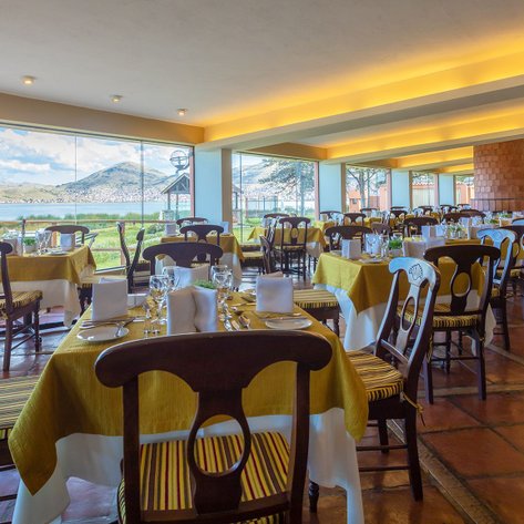 Ein elegantes Restaurant mit Tischen, die mit gelben Tischdecken und Gläsern gedeckt sind, bietet einen Blick auf den See.