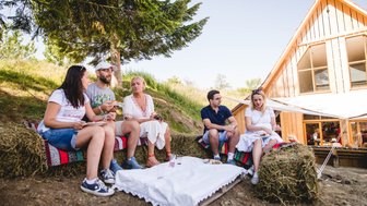 Eine Gruppe von fünf Freunden sitzt entspannt auf Heuballen und genießt ein Picknick in der ländlichen Umgebung.