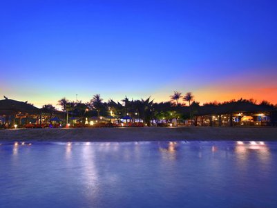 Ein malerischer Sonnenuntergang über einem Strand mit Palmen und einem einladenden Resort im Hintergrund.