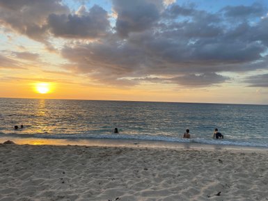 Ein Sonnenuntergang über dem Meer, während Menschen im Wasser planschen und die ruhige Atmosphäre genießen.