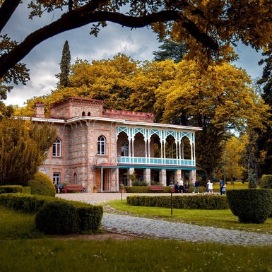 Ein historisches Gebäude mit blauen Verzierungen steht umgeben von bunten Bäumen und einem gepflegten Garten.