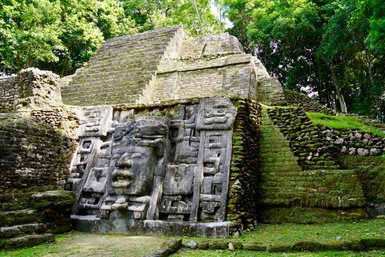 Die beeindruckenden Lamanai-Ruinen zeigen eine massive Steinskulptur mit einem Gesicht, umgeben von üppigem Grün.