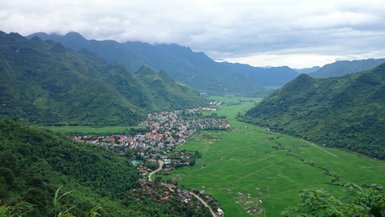 Ein malerischer Blick auf ein Dorf, umgeben von üppigen grünen Bergen und weitläufigen Reisfeldern.