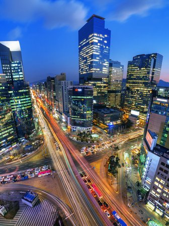 Die Stadt Seoul erstrahlt in der Dämmerung, mit leuchtenden Wolkenkratzern und lebhaften Straßen voller Autos.