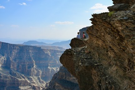 Kind und Teenager sitzen auf einem großen Felsen und genießen den Panoramablick über die Schluchten des Jebel Shams – Oman Reise mit Kindern