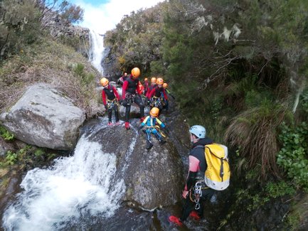 Eine Gruppe von Canyoning-Abenteurern steht an einem Wasserfall, bereit, den nächsten Abschnitt des Flusses zu erkunden.