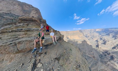 Familie macht eine Pause auf einem Felsen und blickt über die beeindruckende Schlucht des Jebel Shams – Oman mit Kindern