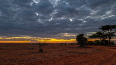 Ein atemberaubender Sonnenuntergang über der kenianischen Savanne, mit dramatischen Wolken und orangefarbenem Himmel.