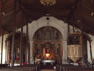 Das Innere einer alten Kirche zeigt einen beeindruckenden Altar mit kunstvollen Details und einem leuchtenden Kerzenlicht.