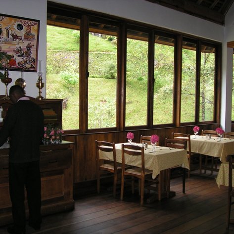 Ein Restaurant mit Holzmöbeln, in dem ein Kellner an einem Tisch arbeitet, während die Natur durch große Fenster sichtbar ist.