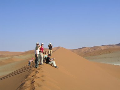 Eine Reisegruppe sitzt entspannt auf einer Sanddüne und genießt die Aussicht - Namibia Rundreise mit Kindern