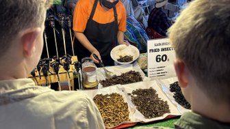 Zwei Kinder sehen einem Einheimischen beim Zubereiten von Essen zu - Thailand Familienreise 