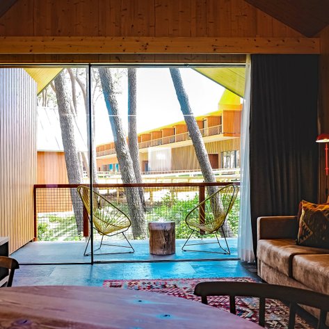 Ein modernes Wohnzimmer mit großen Fenstern, die auf eine grüne Umgebung und Holzarchitektur blicken.