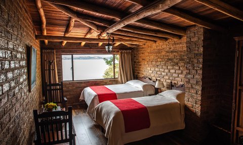 Ein gemütliches Zimmer mit zwei Betten, Holzdecken und einem großen Fenster, das einen Blick auf die Natur bietet.