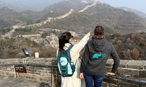 Zwei Frauen stehen auf der Chinesischen Mauer und zeigen auf die beeindruckende Landschaft und die Berge im Hintergrund.