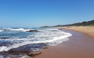Ein ruhiger Strand mit sanften Wellen, die auf den goldenen Sand treffen, unter einem strahlend blauen Himmel.