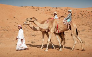 Beduine führt zwei Kamele mit zwei Mädchen durch die Wüste – Oman Familienreise
