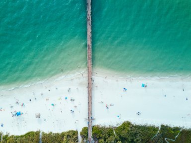 Ein weitläufiger Strand mit feinem, weißen Sand und einem langen Holzsteg, der ins türkisfarbene Wasser führt.