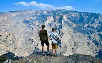 Teenager und Kind blicken gemeinsam auf die atemberaubende Schluchtlandschaft des Jebel Shams – Oman mit Kindern