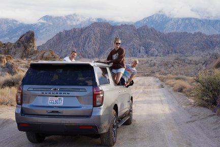 Eine Familie genießt einen Roadtrip in der Wüste, während sie fröhlich aus einem SUV herausblickt.