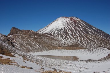 Der schneebedeckte Vulkan erhebt sich majestätisch unter einem klaren blauen Himmel, umgeben von rauem, felsigem Terrain.