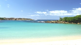 Ein ruhiger Strand mit feinem, hellem Sand und klarem, türkisfarbenem Wasser unter einem strahlend blauen Himmel.