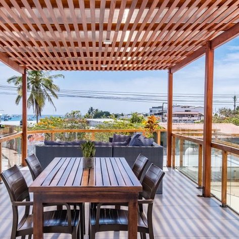 Eine stilvolle Terrasse mit einem Holztisch und Stühlen, umgeben von Palmen und Blick auf das Meer.