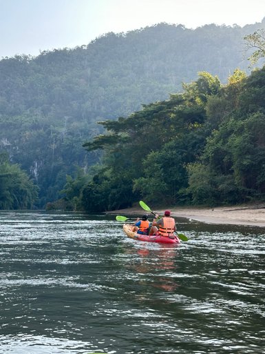 Kind und Erwachsener paddeln im Kanu über ruhigen Fluss in Kanchanaburi - Thailand mit Kindern