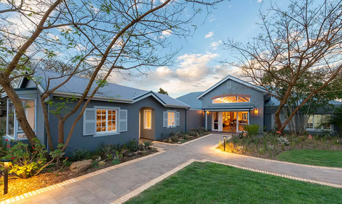 Ein modernes, einladendes Haus mit blauen Wänden und großen Fenstern, umgeben von gepflegtem Grün und sanften Lichtquellen.