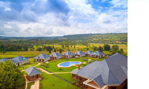 Eine weitläufige Landschaft mit modernen Villen und einem glitzernden Pool, umgeben von sanften Hügeln und bewölktem Himmel.