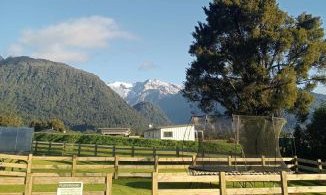 Eine weitläufige Landschaft mit einem Trampolin, umgeben von Zäunen und majestätischen Bergen im Hintergrund.