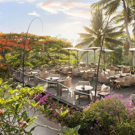 Eine elegante Open-Air-Bar in Bali, umgeben von üppigem Grün und bunten Blumen, bietet eine entspannte Atmosphäre.