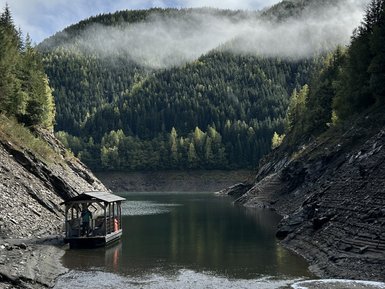 Ein kleines Boot liegt ruhig am Ufer eines klaren Sees, umgeben von majestätischen Bergen und dichten Wäldern.