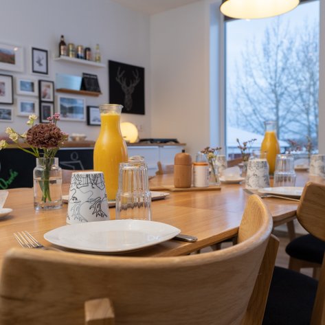Ein einladender Essbereich mit einem großen Holztisch, dekoriert mit Geschirr und frischen Blumen in einer Vase.
