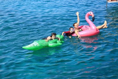 Drei Kinder genießen das Schwimmen im klaren Wasser, während sie auf bunten Luftmatratzen entspannen und lachen.