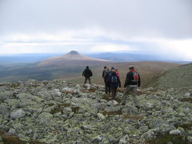 Eine Gruppe von Wanderern erkundet eine felsige Landschaft mit einem markanten Hügel im Hintergrund unter einem bewölkten Himmel.