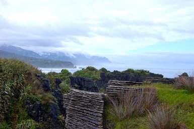 Die beeindruckenden Pancake Rocks in Punakaiki erheben sich majestätisch über die Küste, umgeben von üppigem Grün und sanften Wellen.