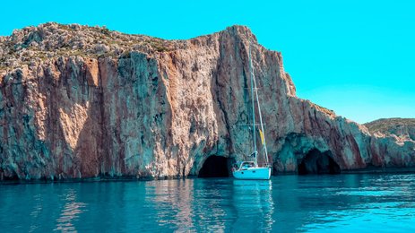 Ein Segelboot schaukelt sanft auf dem glitzernden Wasser, umgeben von majestätischen, steilen Klippen und klarem Himmel.