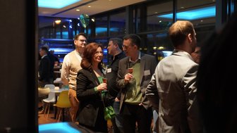 Eine Gruppe von Menschen unterhält sich in einer stilvollen Bar, während sie Getränke in der Hand halten und lächeln.