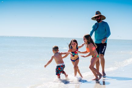Ein Vater spielt mit seinen Kindern am Strand, während sie fröhlich im Wasser planschen und lachen.