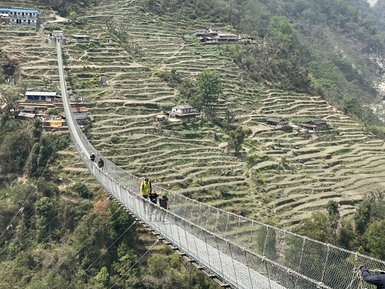 Eine schmale Hängebrücke verbindet zwei Berghänge, während Wanderer über die beeindruckende Landschaft gehen.