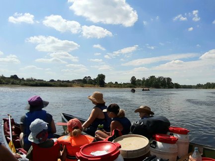 Eine Gruppe von Menschen sitzt in einem Kanu und genießt einen sonnigen Tag auf einem ruhigen Fluss mit blauen Himmel.