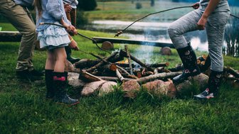 Eine Gruppe von Kindern steht um ein Lagerfeuer, während sie mit Stöcken über die Flammen braten.