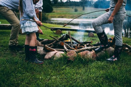 Eine Gruppe von Kindern steht um ein Lagerfeuer, während sie mit Stöcken über die Flammen braten.