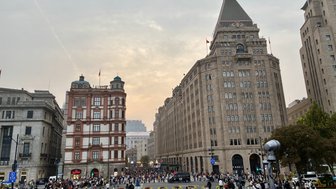Eine belebte Straße in Shanghai, umgeben von historischen Gebäuden und einer großen Menschenmenge, die sich versammelt.