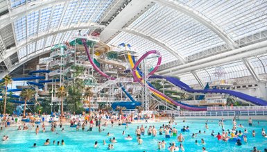 Ein lebhaftes Wasserpark-Szenario mit vielen Menschen, die im Wasser spielen und auf Rutschen rutschen.