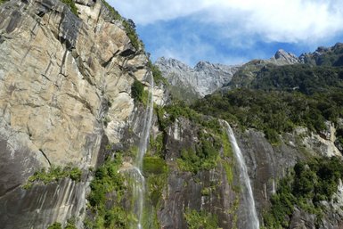 Majestätische Wasserfälle stürzen von steilen Klippen in das grüne Tal, umgeben von beeindruckenden Bergen und klarem Himmel.
